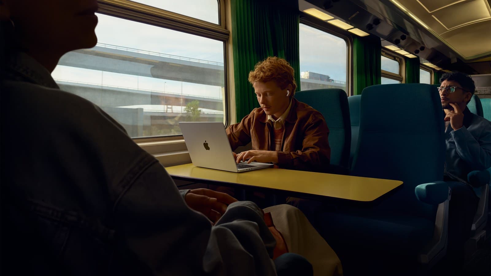 Jeune homme travaillant sur un MacBook dans un train avec des AirPods Pro 3