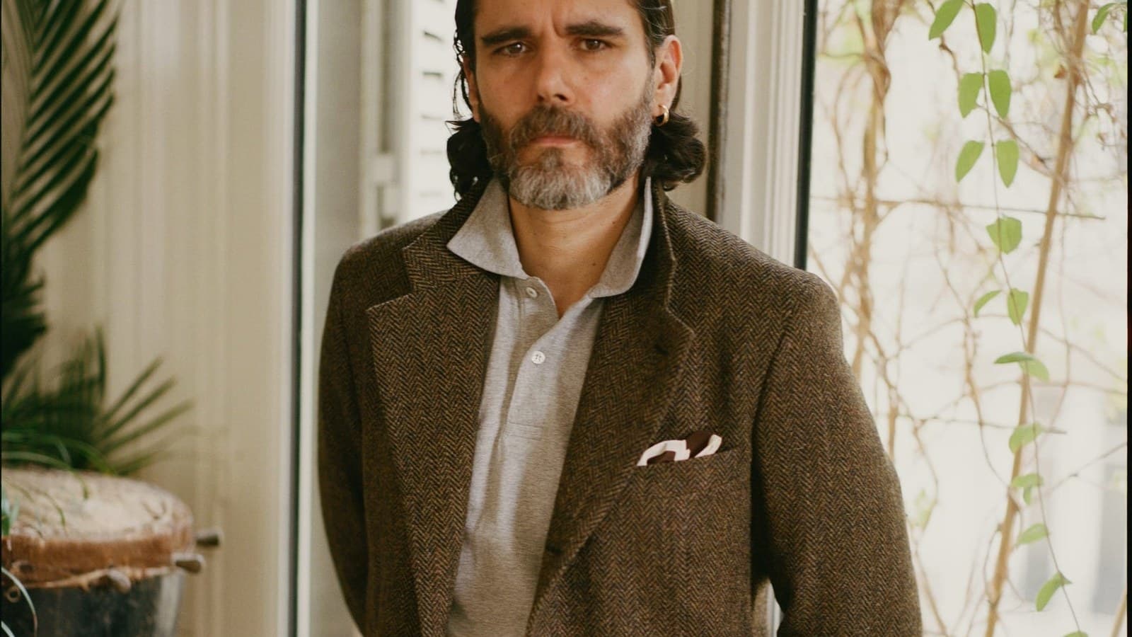 Homme en veste de tweed et chemise ouverte, pochette blanche, dans un intérieur parisien