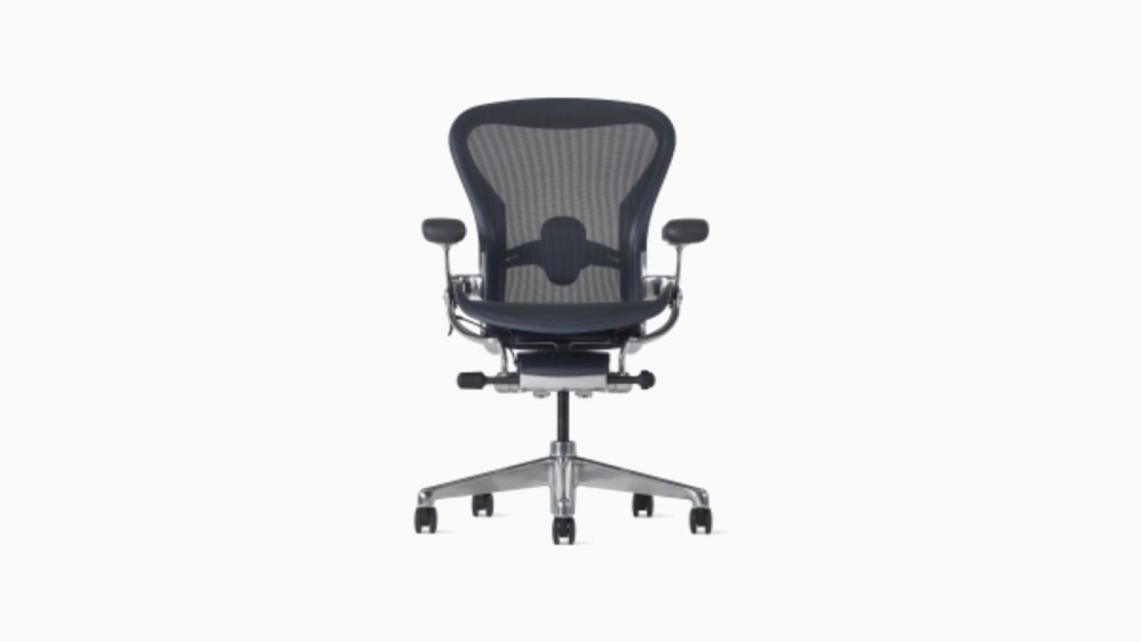 Fauteuil de bureau en maille noire vu de trois quarts devant un bureau en bois clair, accoudoirs réglés en position basse