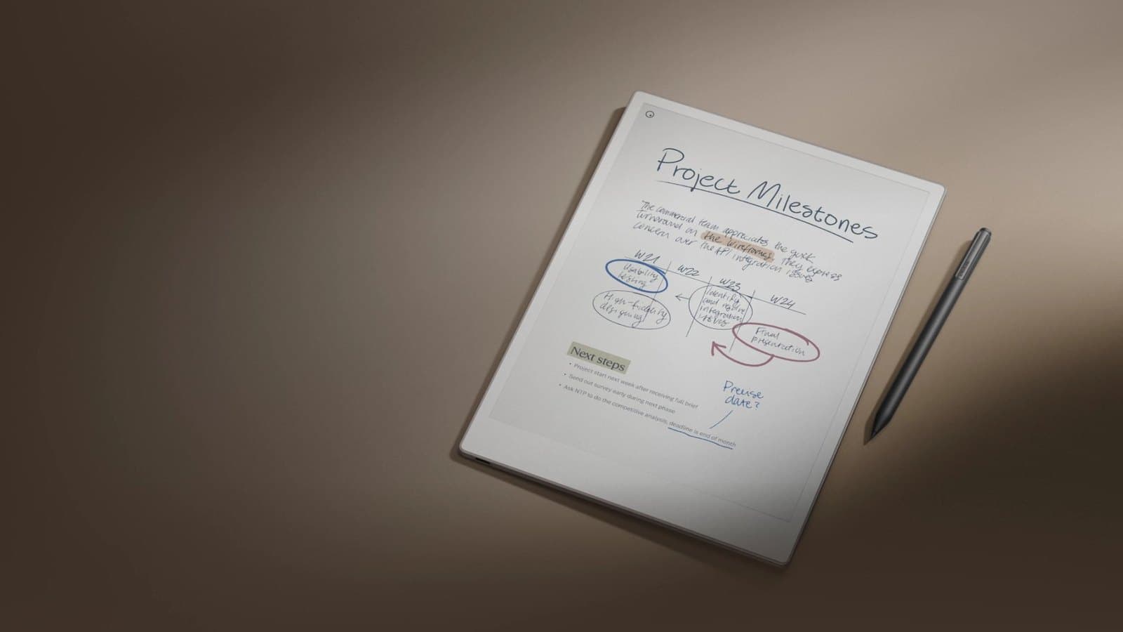 Tablette d'encre électronique posée sur une table de réunion en bois clair, stylet à côté, page manuscrite affichée avec un tableau dessiné à la main, tasse de café et carnet papier fermé en arrière-plan.