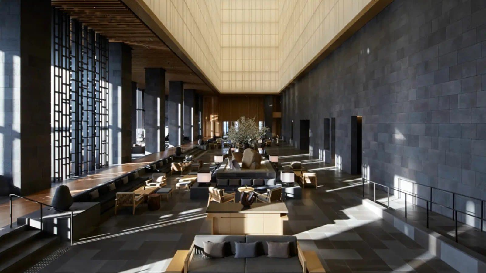 Vue depuis le lobby vitré d'un hôtel au 33e étage, avec un plafond de bois clair très haut et les tours de bureaux de Tokyo au second plan