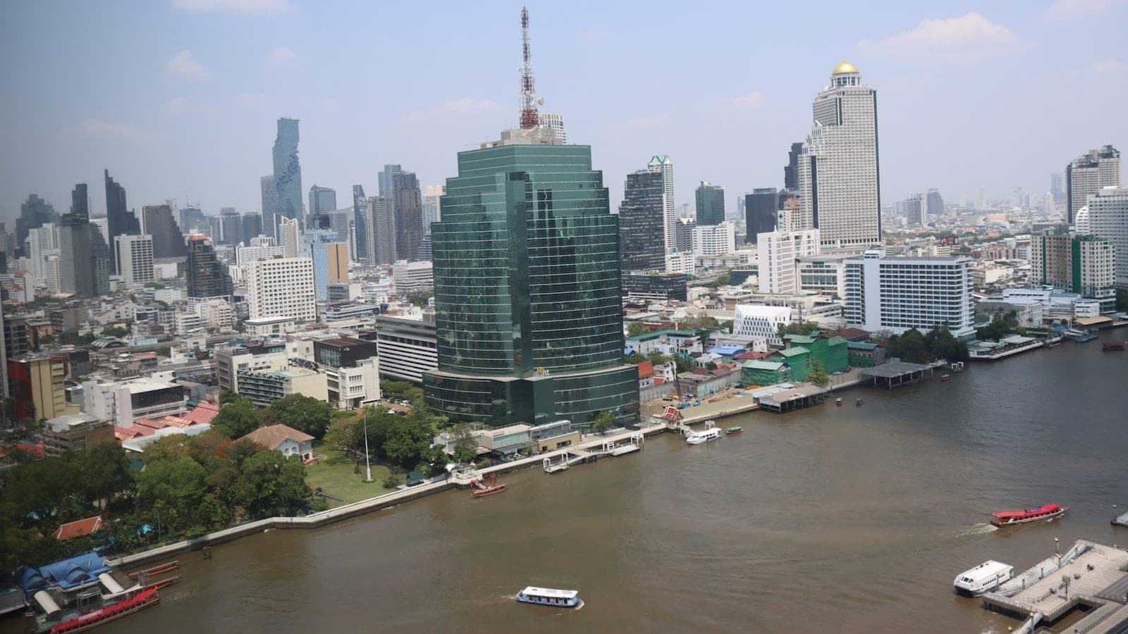 Vue plongeante sur un carrefour de Sathorn à Bangkok en fin de journée, avec une rame du BTS Skytrain sur son viaduc et des files de voitures à l'arrêt en dessous.