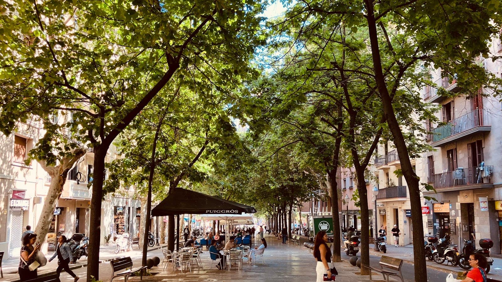 Vue plongeante sur un croisement en damier de l’Eixample à Barcelone en fin de matinée, taxis noir et jaune arrêtés au feu et terrasses de café sur les angles coupés.