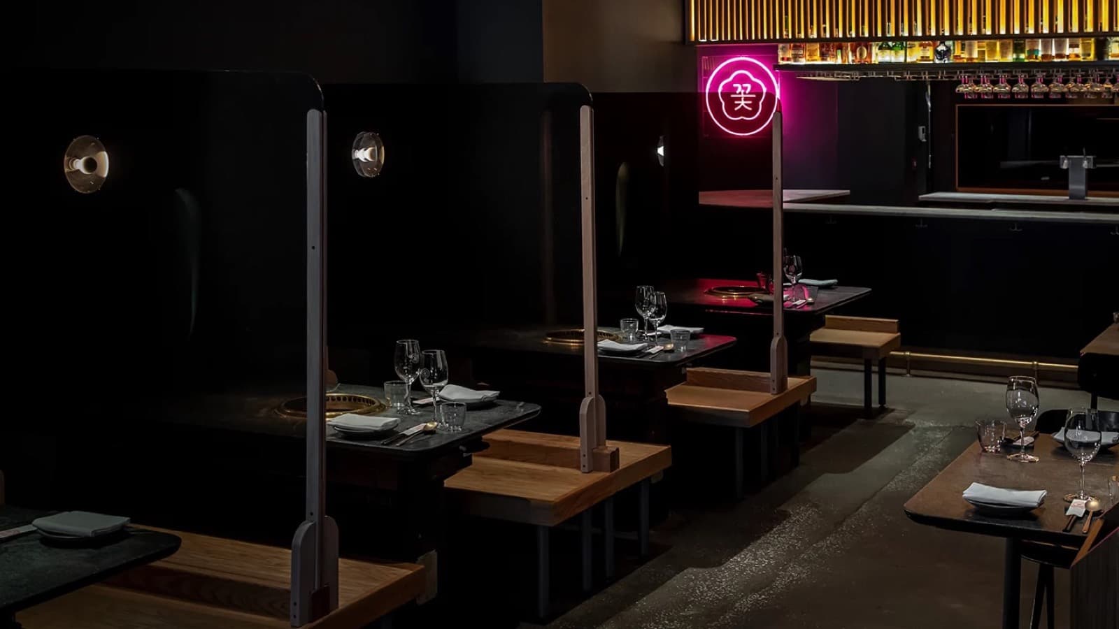 La salle sombre de COTE à Flatiron, tables équipées de grilles dorées et néon rose au logo de la maison au dessus du bar