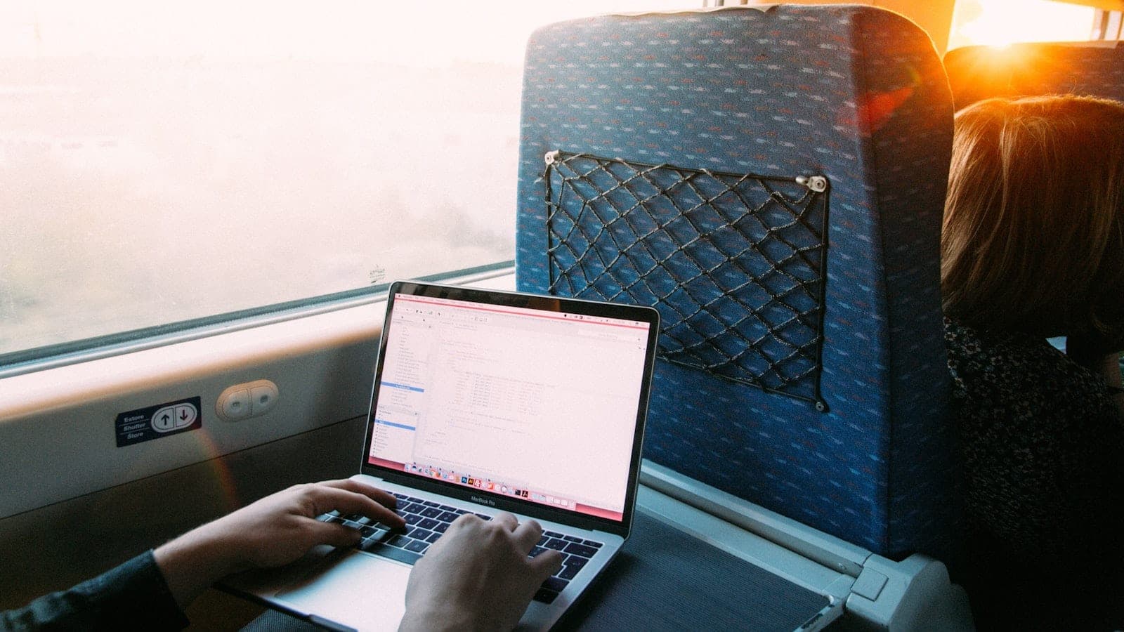 Ordinateur portable ouvert sur une tablette de siège d'avion, écran affichant un terminal et un éditeur de texte, hublot fermé et lampe de lecture allumée.