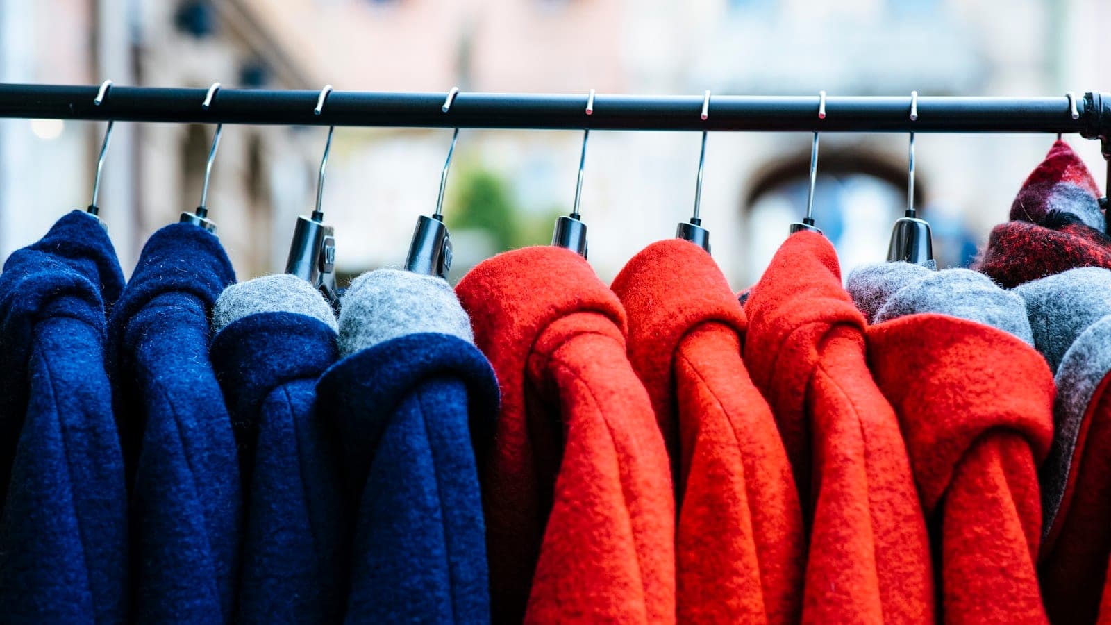 Manteau en laine gris anthracite posé plié sur une valise cabine rigide, dans un hall d'aéroport, avec une balance de bagage accrochée à la poignée