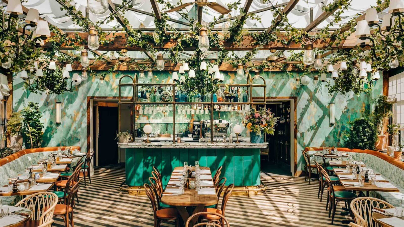 La salle sous verrière de Pink Mamma, carrelage vert, banquettes et plantes suspendues
