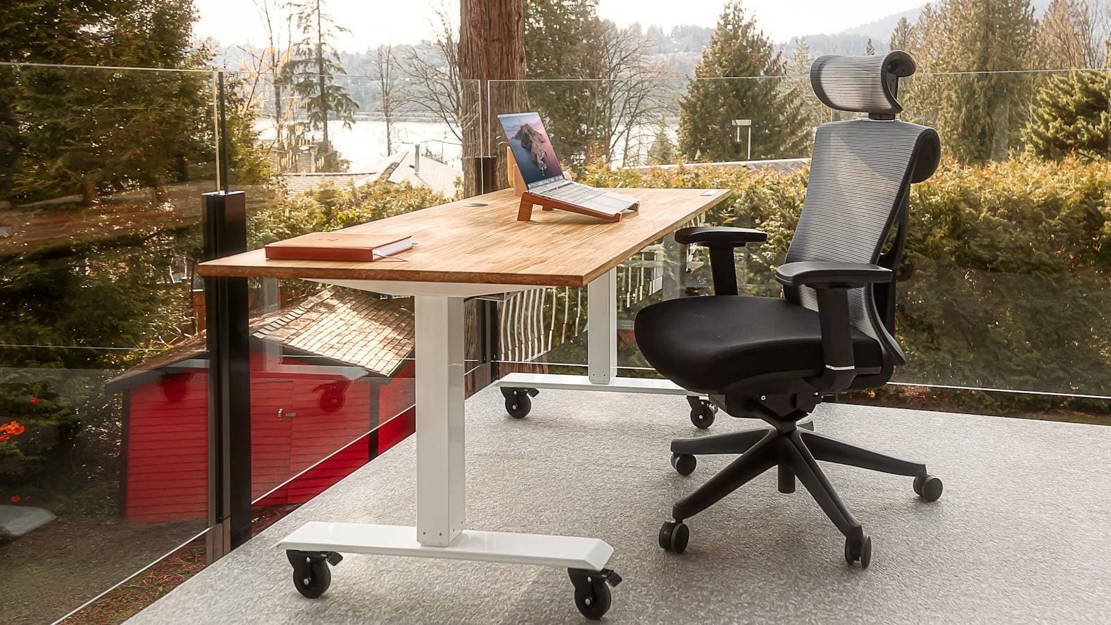 Bureau assis-debout en bois clair et fauteuil ergonomique a appui-tete, face a une baie vitree