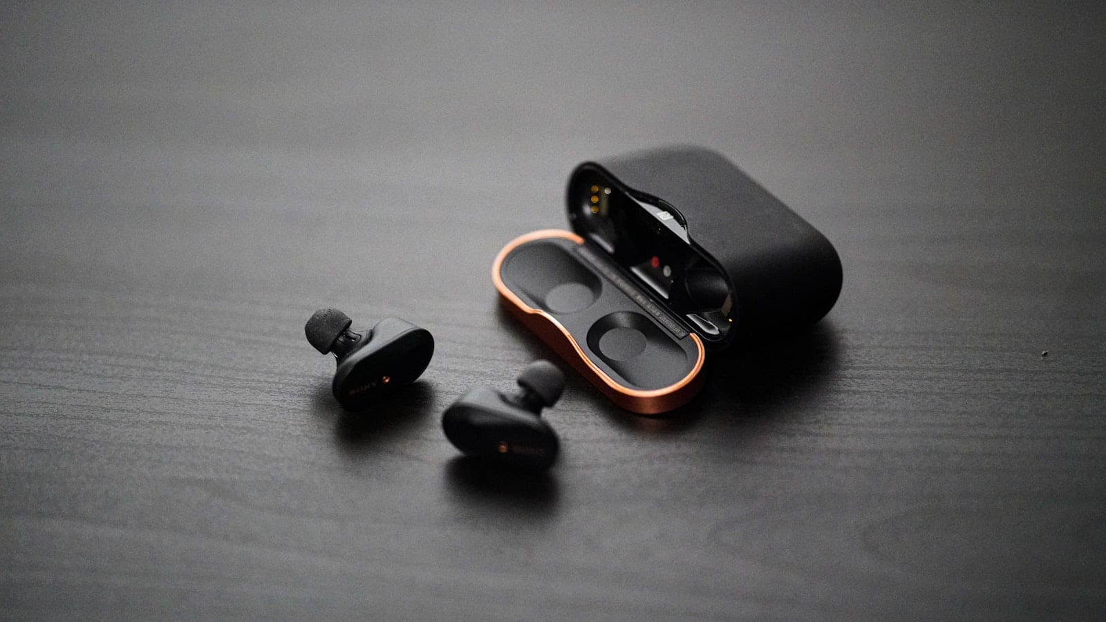 Cinq paires d'écouteurs intra-auriculaires posées sur une tablette de siège d'avion, boîtiers ouverts, hublot en arrière-plan