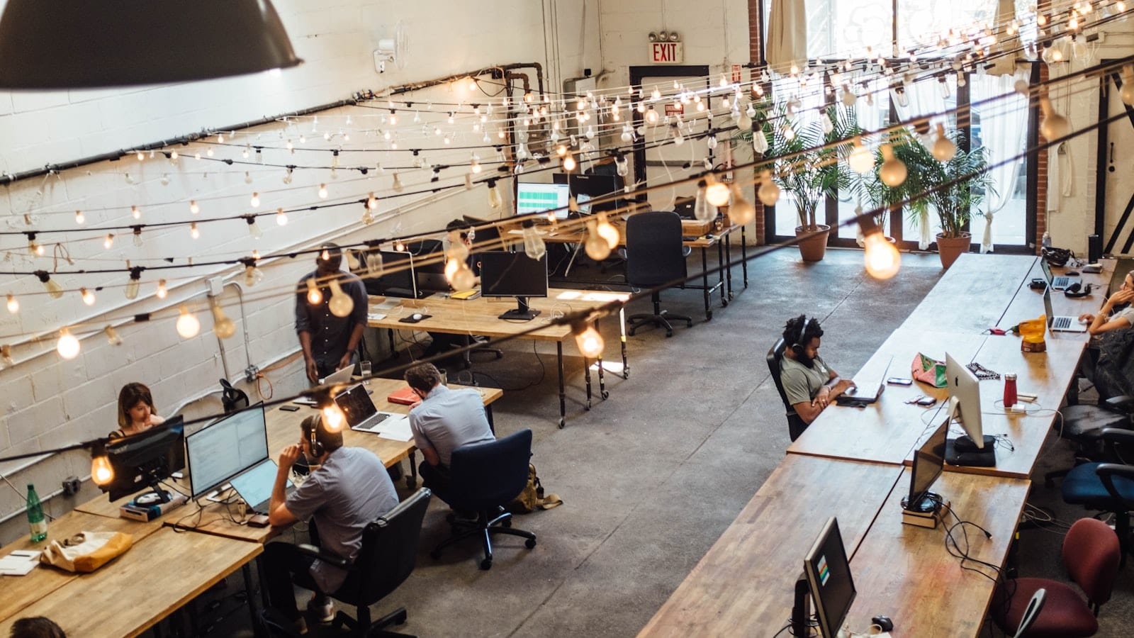 Poste de travail individuel dans un club de travail londonien, ordinateur portable ouvert, tasse de café et cabine visio vitrée en arrière-plan