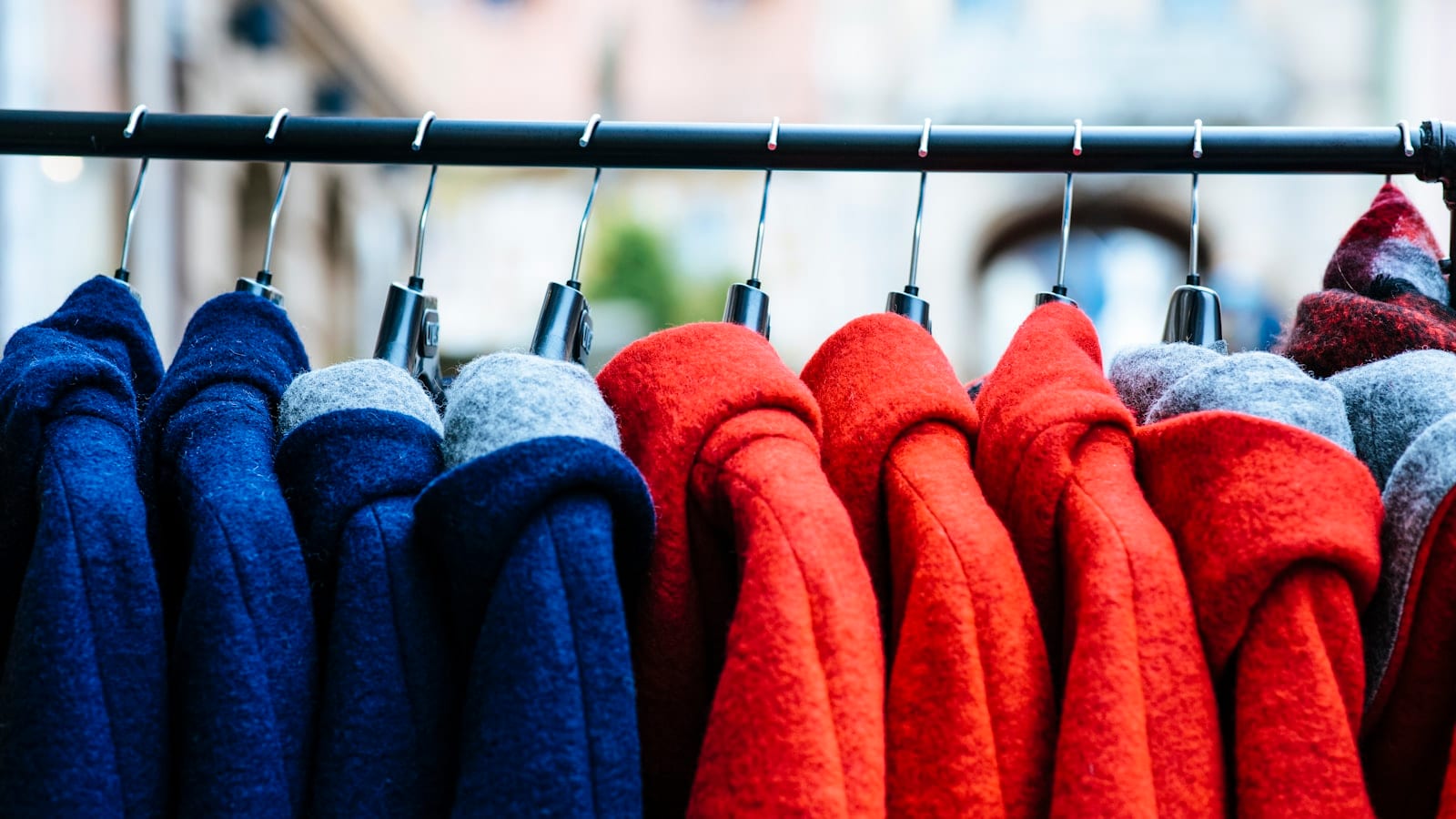Manteau en laine gris anthracite posé plié sur une valise cabine rigide, dans un hall d'aéroport, avec une balance de bagage accrochée à la poignée