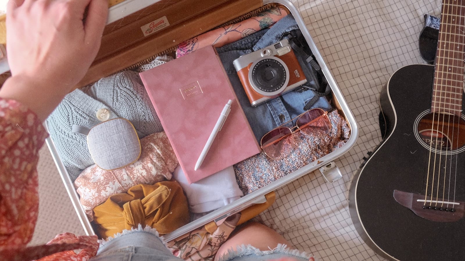 Sac de voyage souple ouvert sur une table, trousse de toilette fermée, adaptateur universel et câbles regroupés dans une pochette, chemise blanche pliée à côté
