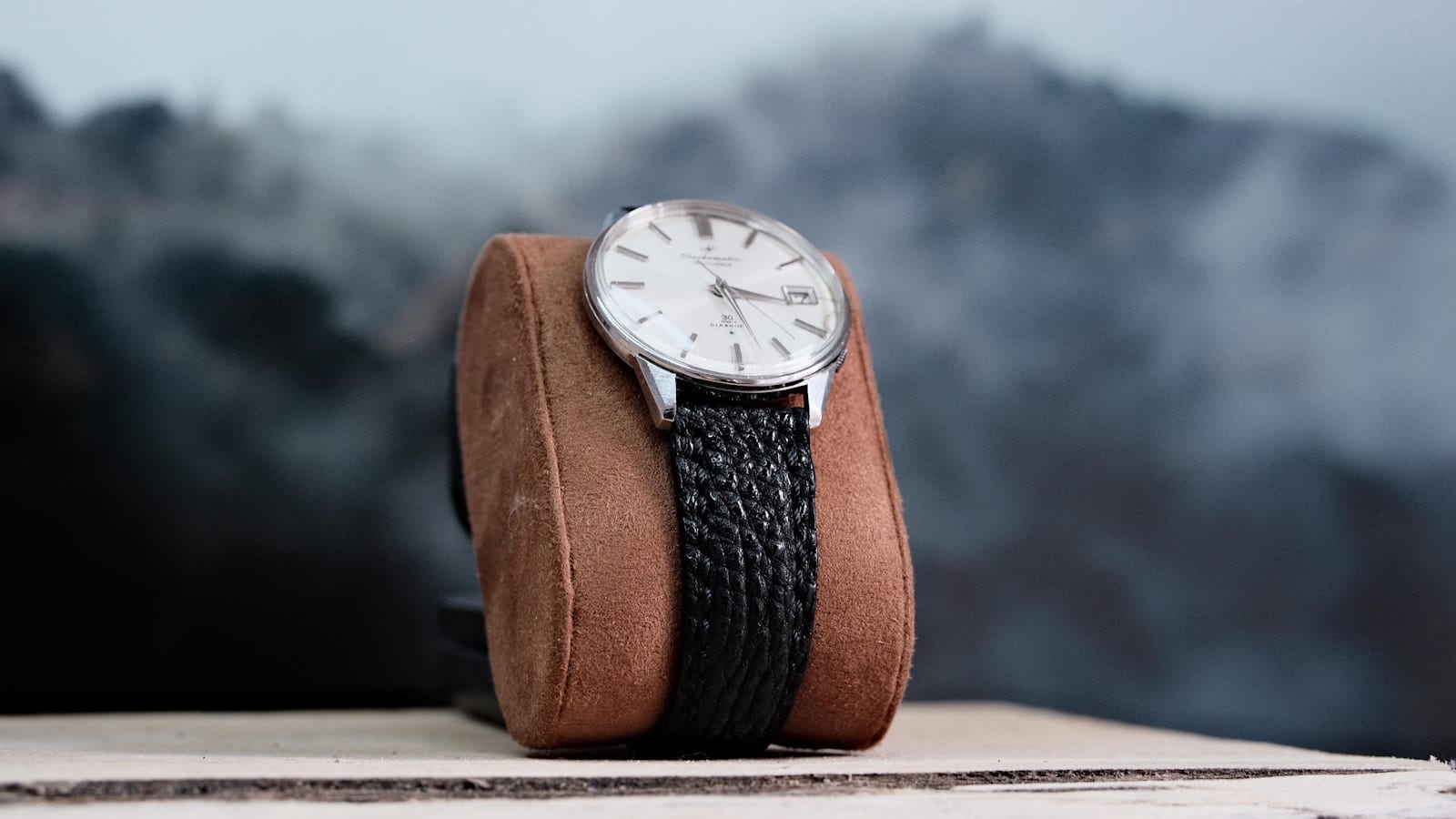 Une montre acier posée à côté d’un passeport, d’une facture d’achat et d’un carnet ouvert sur une page d’inventaire manuscrite, sur un bureau d’hôtel.