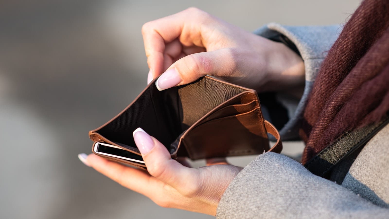 Six portefeuilles slim en cuir et en aluminium disposés en éventail sur une table en bois, cartes bancaires et billets pliés à côté