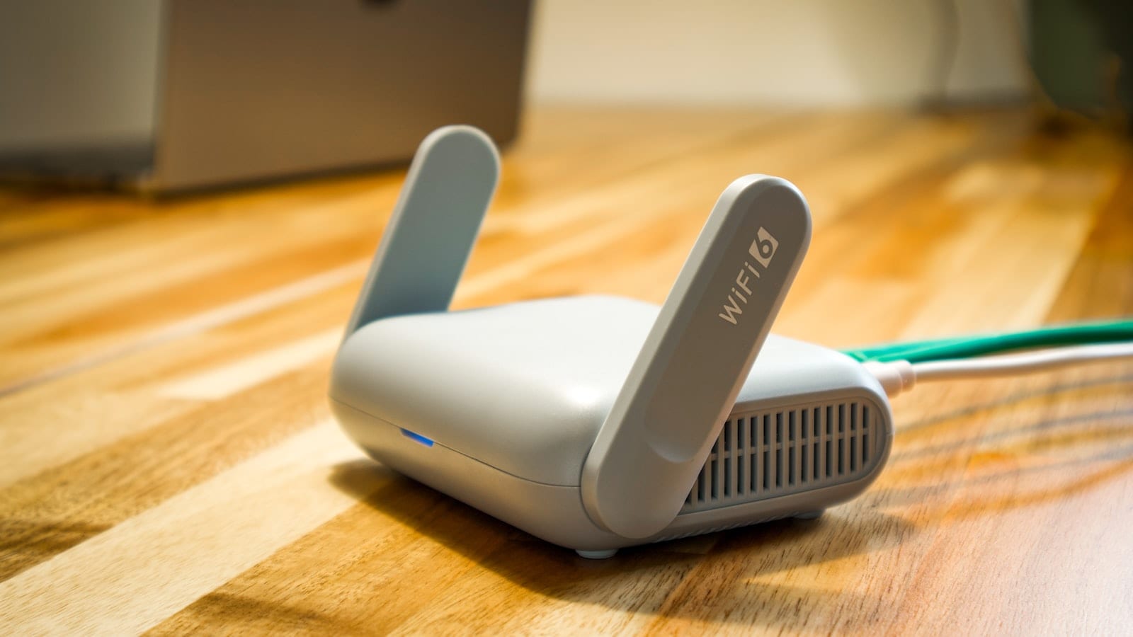 Petit routeur de voyage bleu posé sur un bureau de chambre d'hôtel, relié à une batterie externe par un câble USB-C