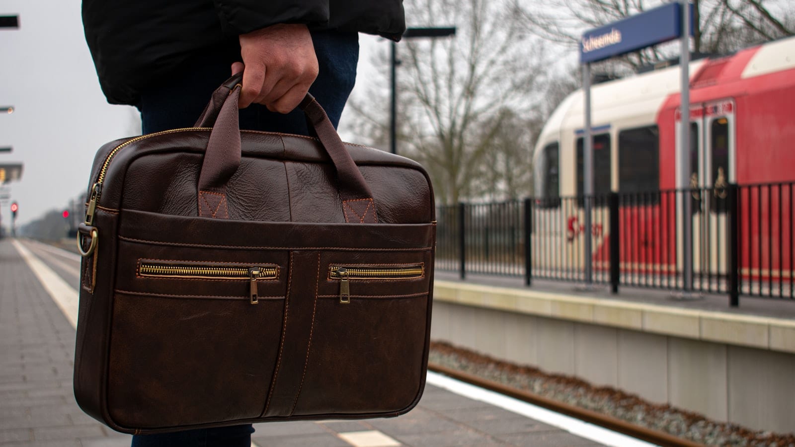 Trois sacs pour ordinateur portable ouverts à plat sur une table en bois clair, un MacBook Pro 16 pouces glissé dans le compartiment suspendu du modèle central, mètre ruban et balance posés à côté.