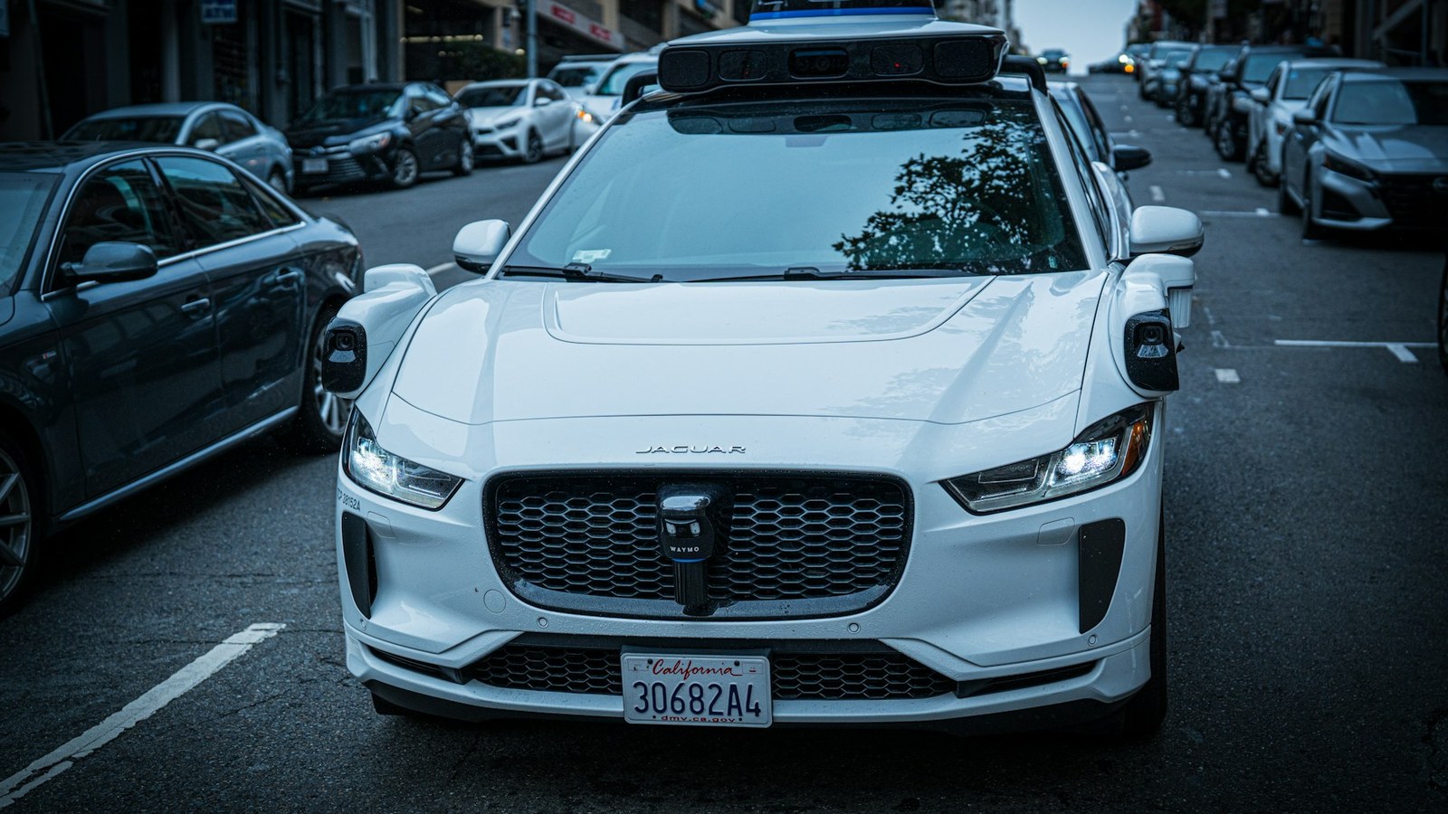 Voiture autonome blanche à capteurs de toit arrêtée dans une rue de ville