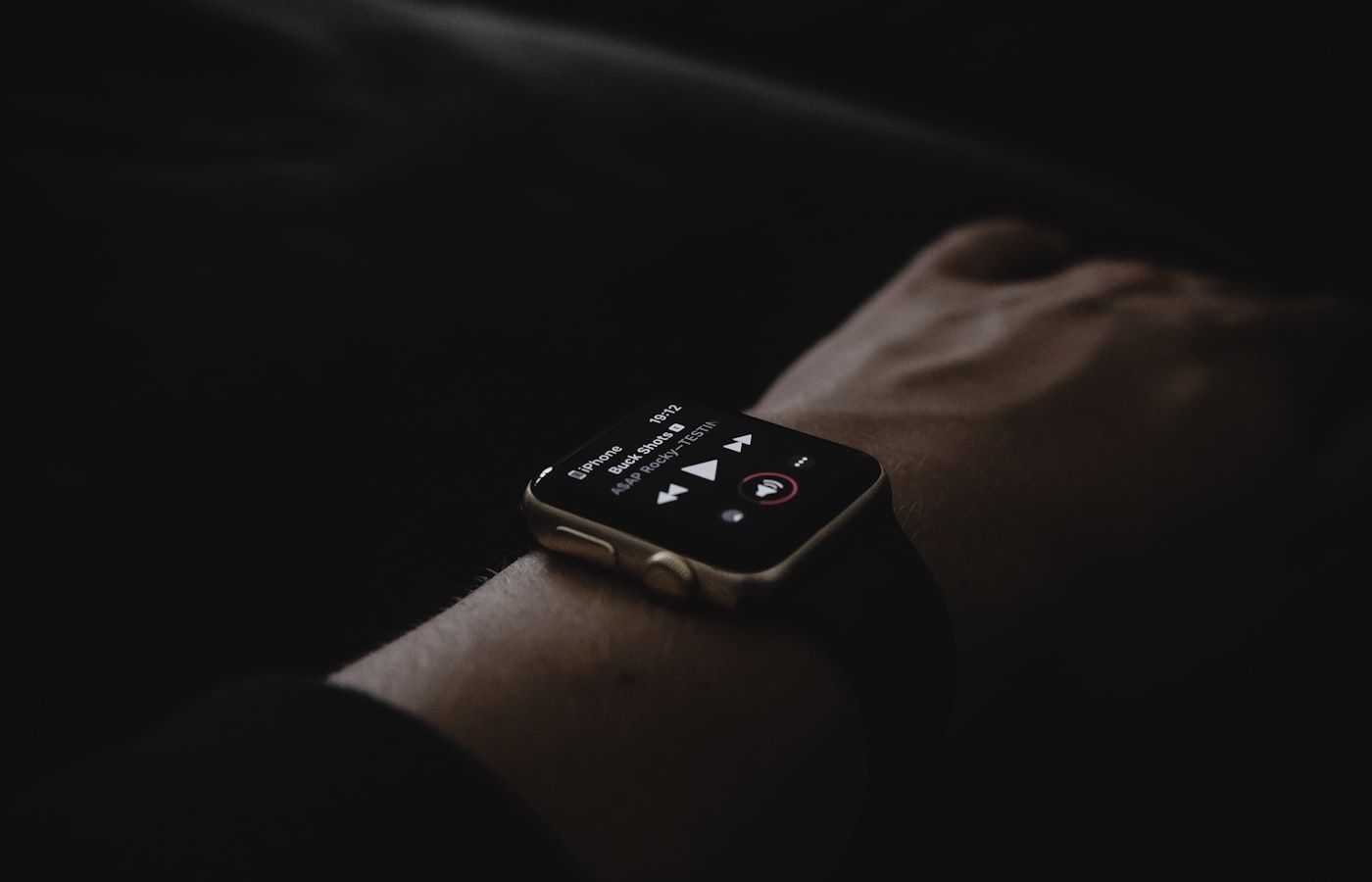 Une valise rigide ouverte sur un lit d'hôtel, avec trois traceurs Bluetooth de formats différents posés sur une pochette en tissu, à côté d'une carte d'embarquement.